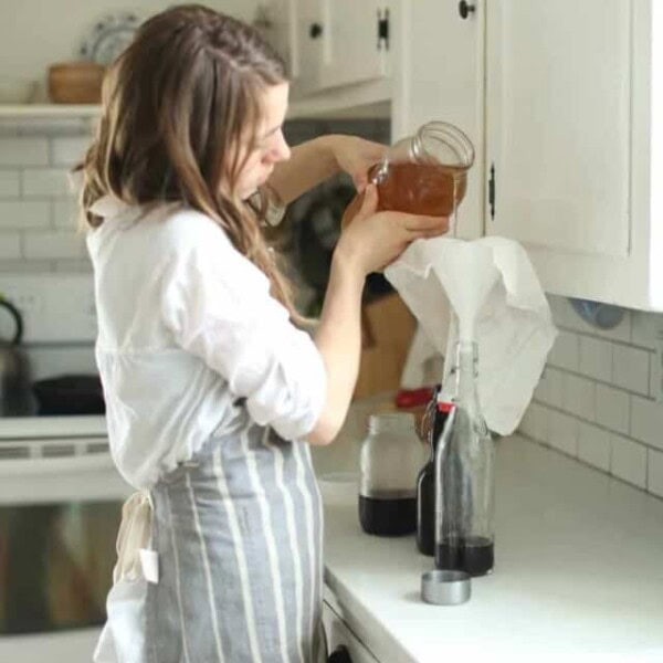 woman pouring water kefir into a flip top bottle in a white kitchen