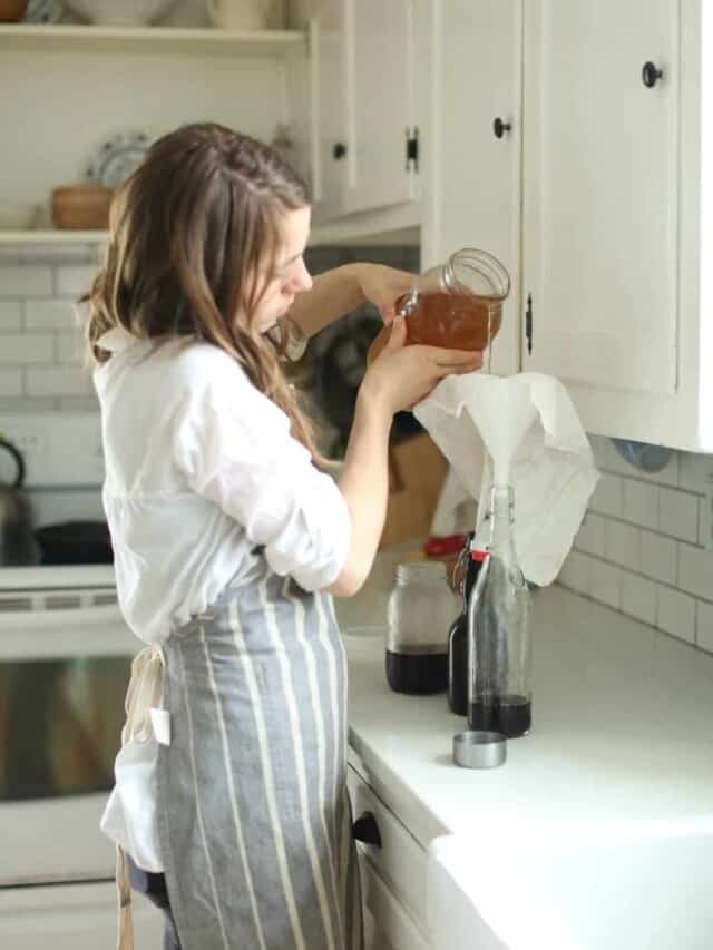 woman pouring water kefir into a flip top bottle in a white kitchen