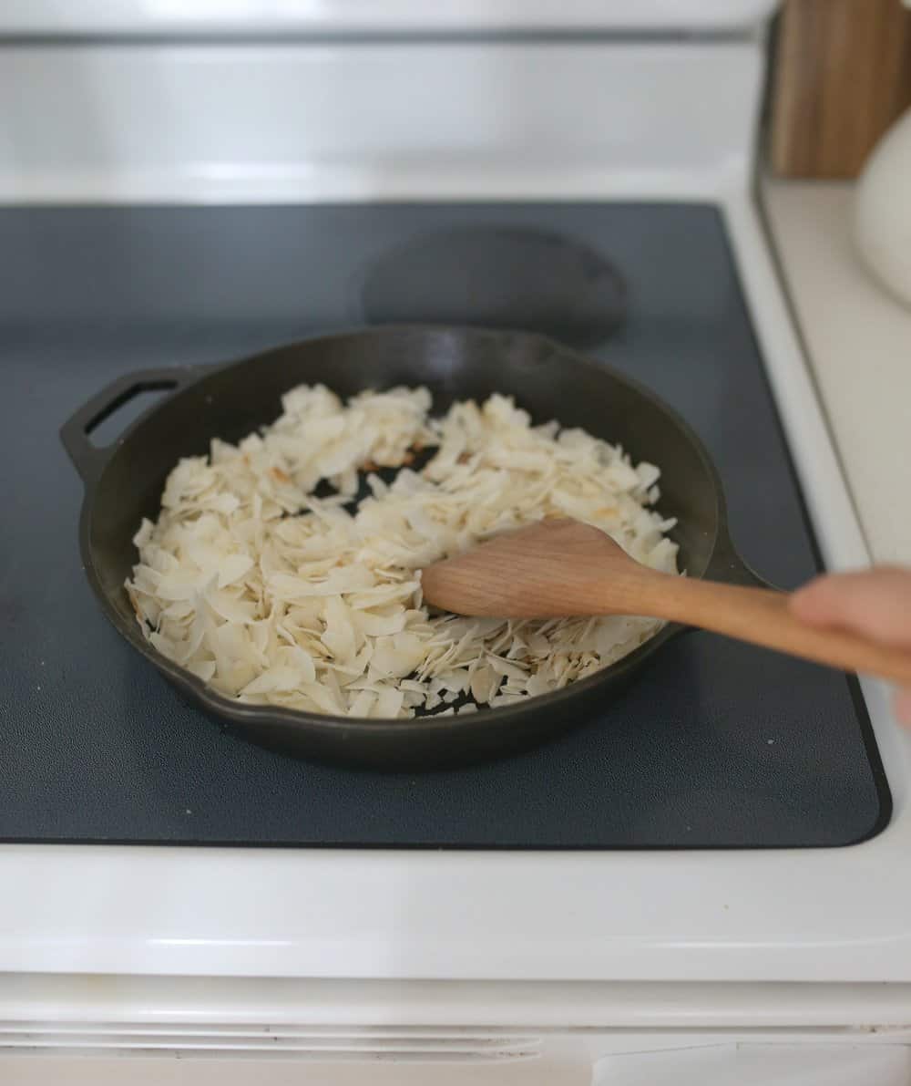 wooden spoon stirring coconut flakes on a cast iron skillet
