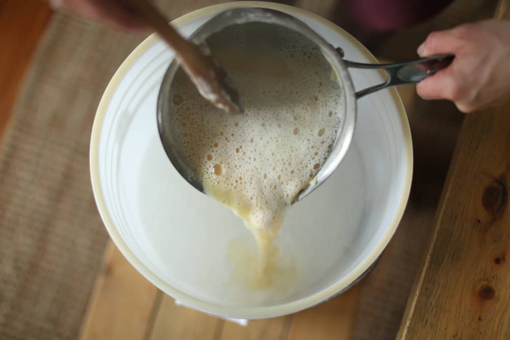 sauce pan of melted Fels Naptha soap and water is being poured into a 5 gallon bucket.