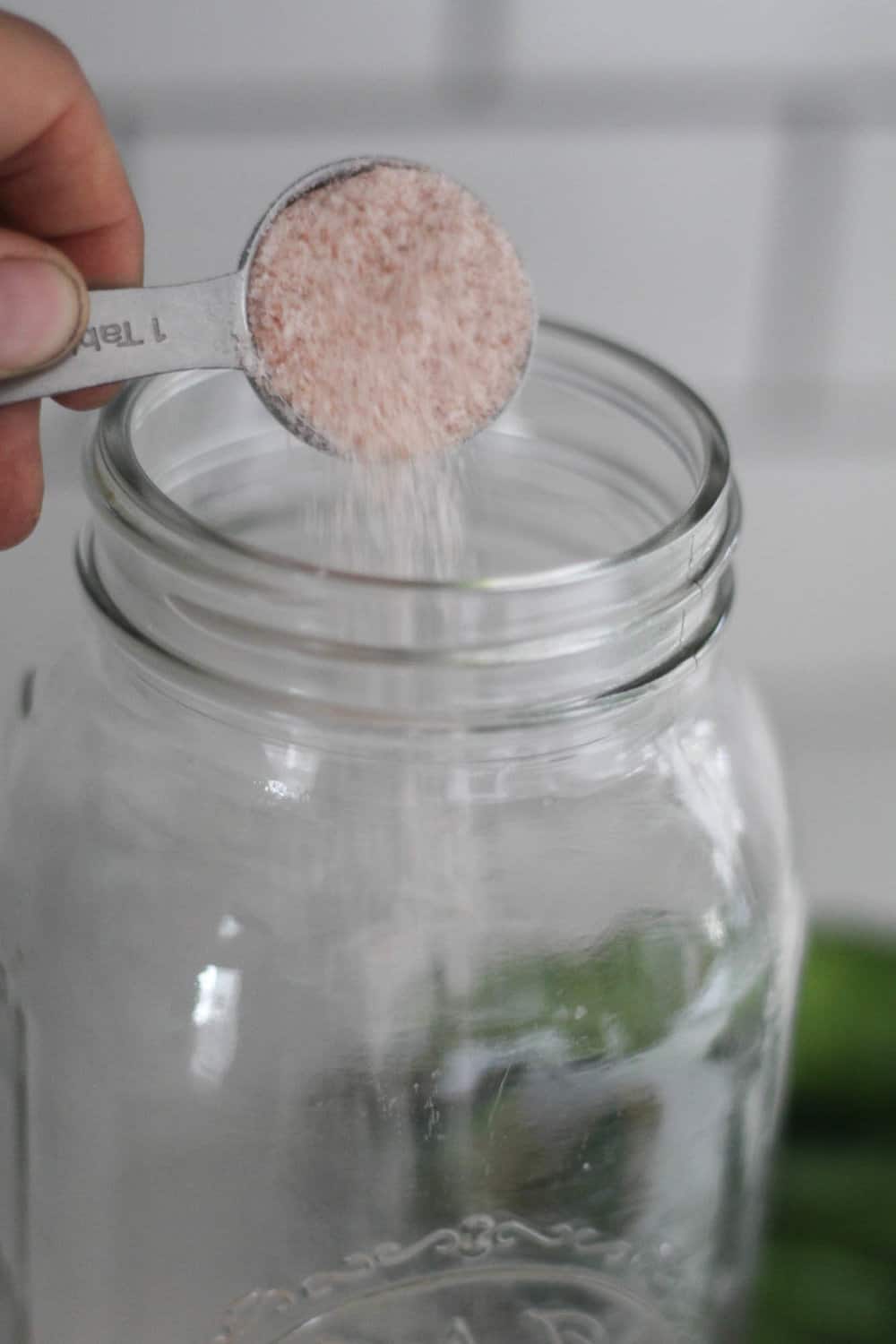 adding pink Himalayan salt into a mason jar to make fermented pickles