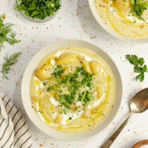 Two bowls of potato soup with a bowl of herbs to top it with next to them.