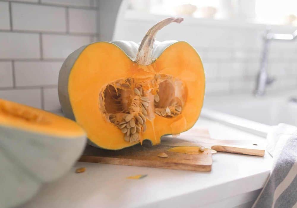 A pumpkin cut in half on a cutting a board.