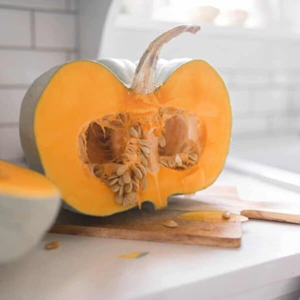 A pumpkin cut in a half on a wooden cutting board.