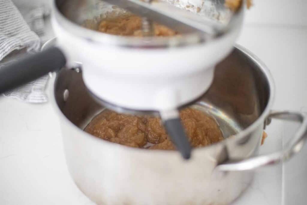 Milling cooked apples through a food mill into a pot.