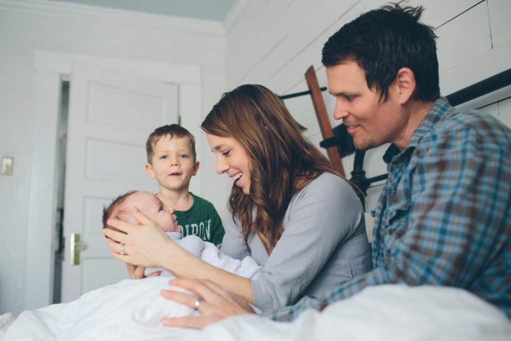 a women sitting in bed holding her baby I front of her with her husband to the right and her older son to the left of her