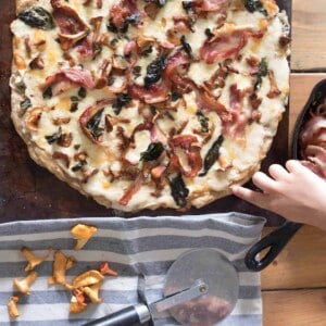 overhead shot of bacon chanterelle mushroom pizza on a pizza stone with ingredients surrounding itforaging chantrelle mushrooms wild edibles