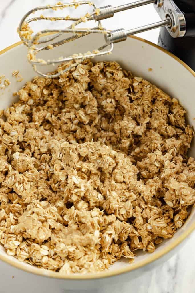 Oats added to the granola cookie dough in a bowl with a hand mixer.