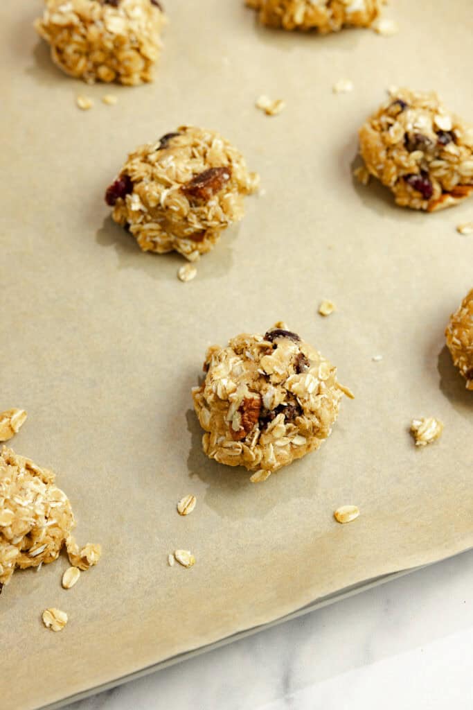 Spoonfuls of granola cookie dough on a parchment paper lined baking sheet.