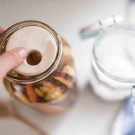 A woman's hand placing a fermenting weight on top of a jar full of carrots in a salt water brine.