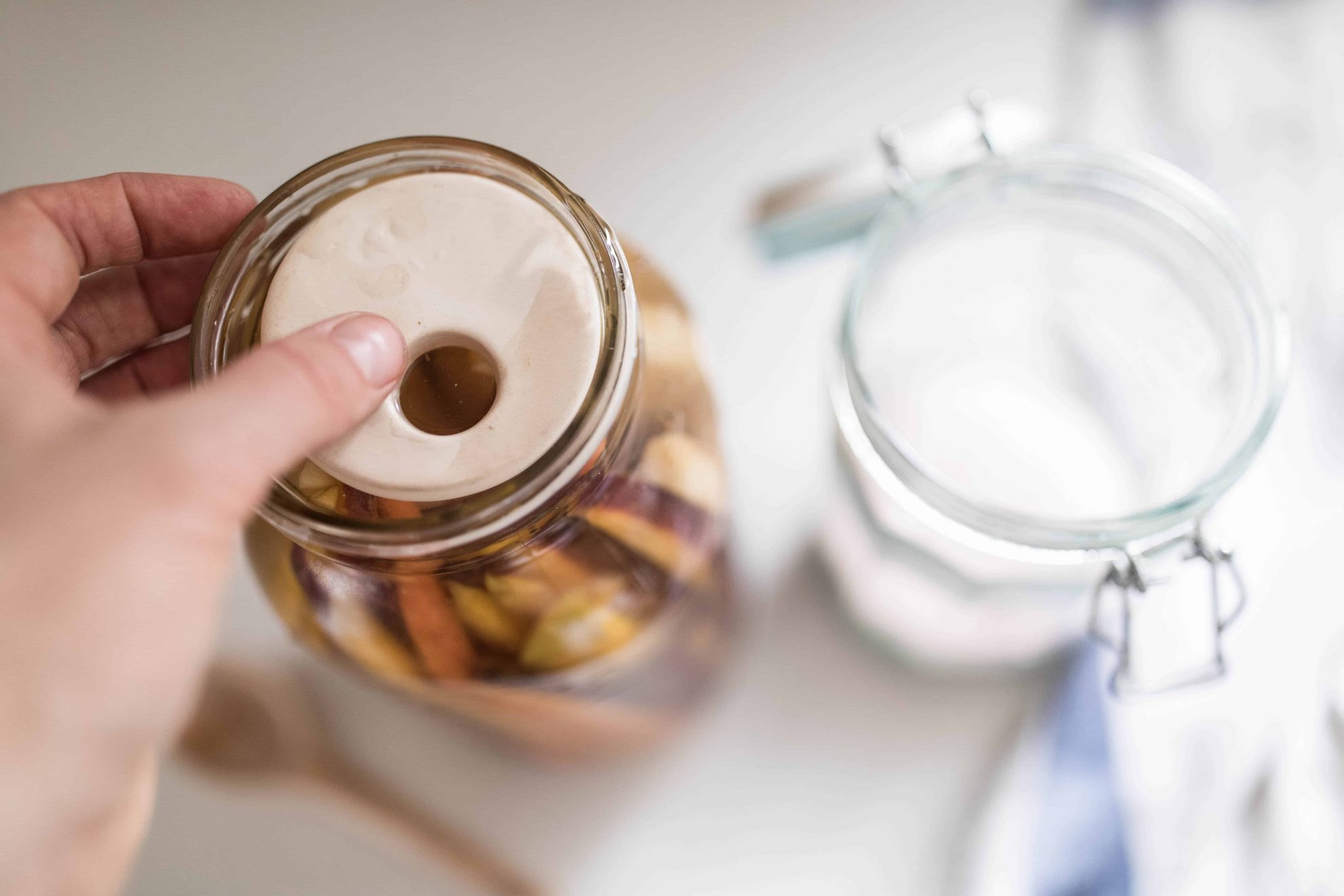 A woman's hand placing a fermenting weight on top of a jar full of carrots in a salt water brine.