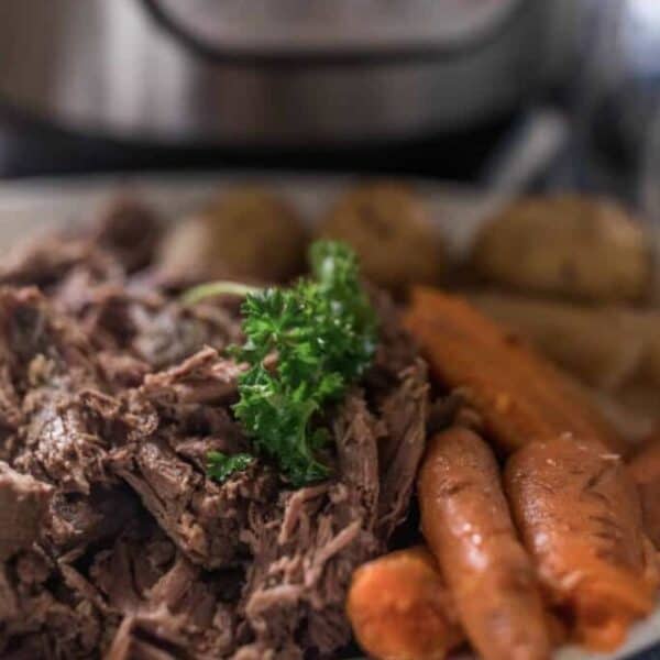 A plate full of beef roast, potatoes and carrots with an instant pot in the background.