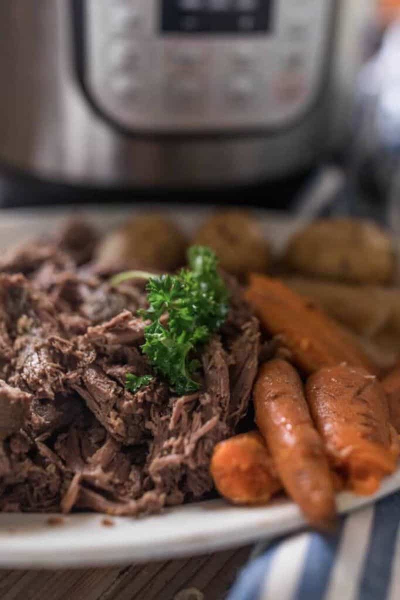 A plate full of beef roast, potatoes, and carrots with an instant pot in the background.