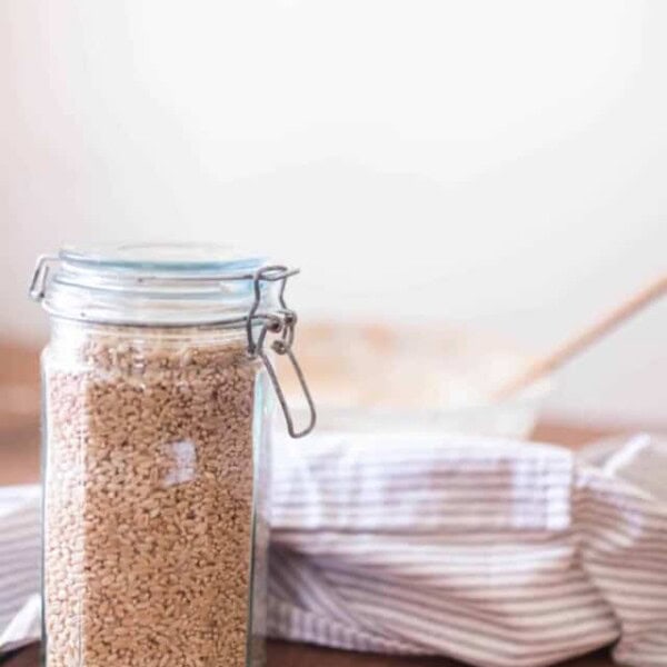 jar with a swing top lid full of wheat berries on a wood table with a bowl and linen stripped towel in the background