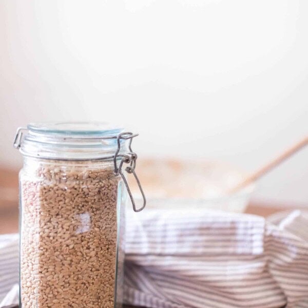 jar with a swing top lid full of wheat berries on a wood table with a bowl and linen stripped towel in the background