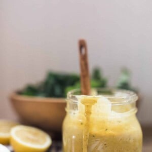 honey mustard dressing in a glass jar with a wooden spoon in the jar and a salad behind it