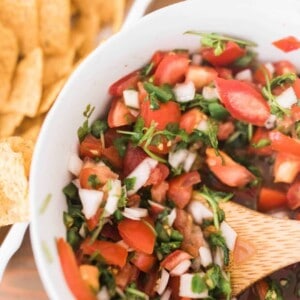 fermented salsa in a white bowl with a wooden spoon surrounded by tortilla chips