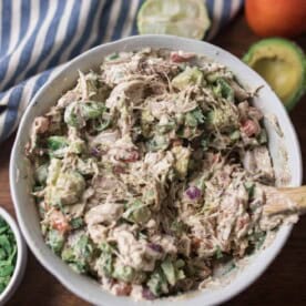 southwest chicken salad in a white bowl with cilantro and avocado around it