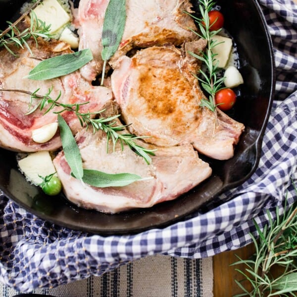 skillet pork chops in a cast iron skillet with fresh herbs on a blue and white towel