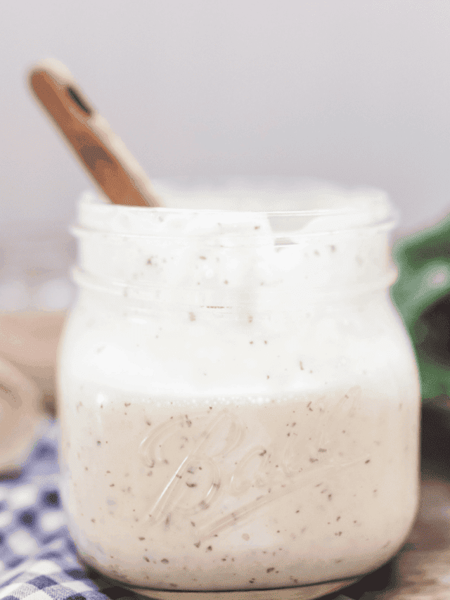 homemade ranch dressing in a mason jar with a wooden spoon in the jar on top a wood table