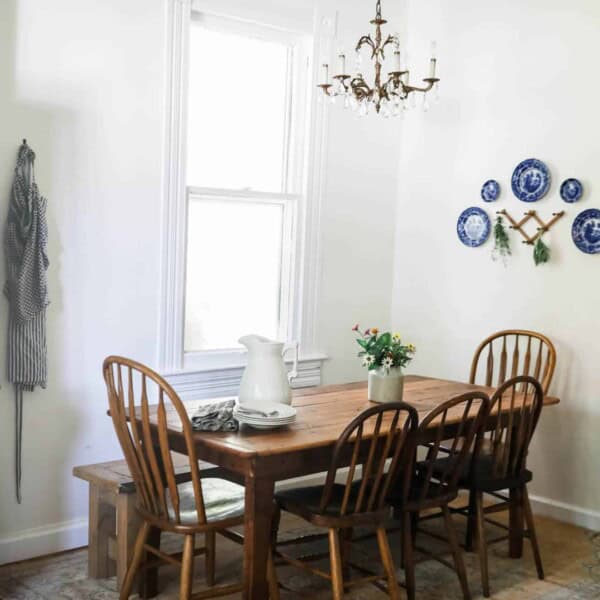 wide shot of farmhouse kitchen table and antique chairs with an antique cabinet full of collected dishes, with a plate wall to the right.