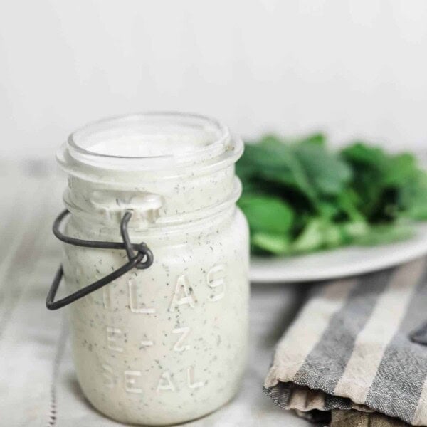 kefir ranch dressing in a vintage mason jar on a striped tea towel with a plate of salad behind it