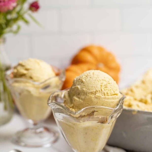 two ice cream cups filled with pumpkin ice cream. Pumpkins and flowers are in the background.