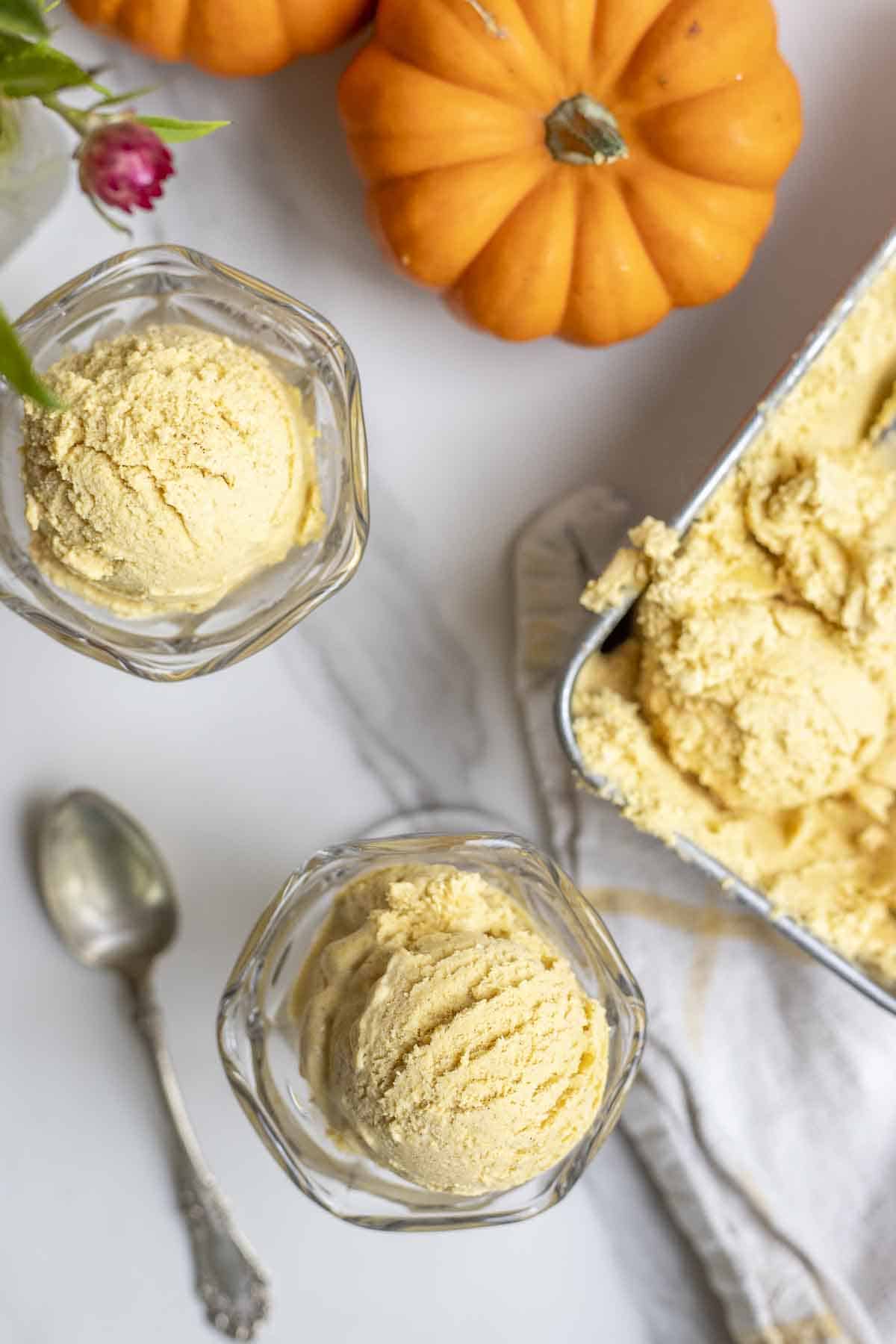 Overhead photo of pumpkin ice cream in Sunday cups on a countertop with pumpkins.