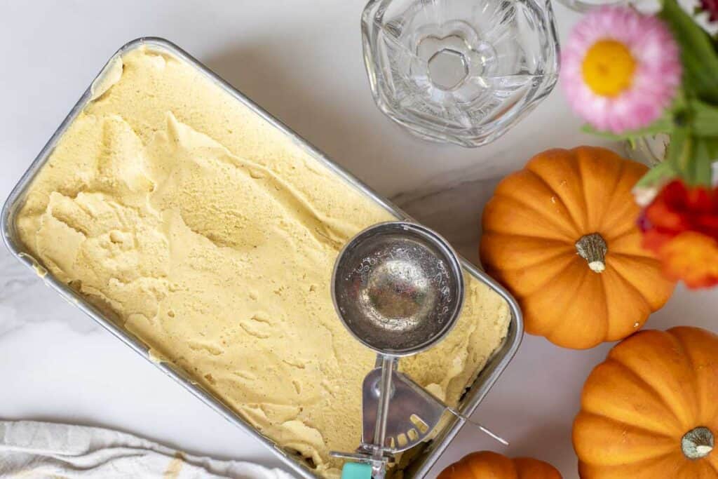 pumpkin ice cream in a loaf pan with a ice cream scoop on top.