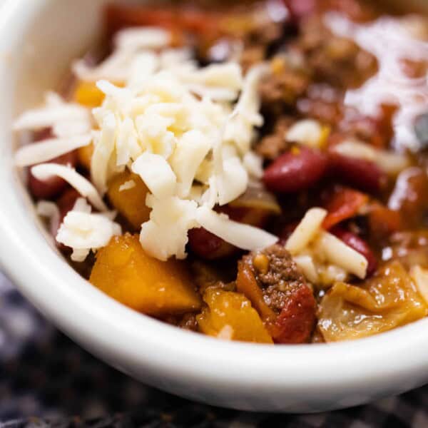 white bowl full of pumpkin chili with ground beef and topped with cheese