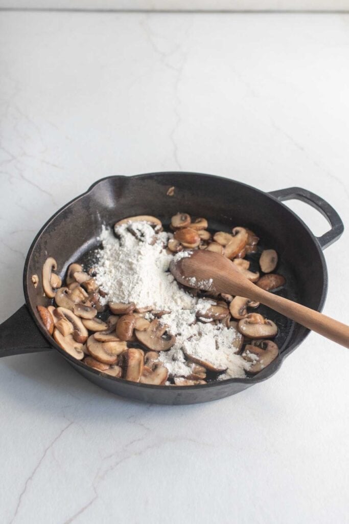 Flour and sauted mushrooms in a cast iron pan, stirred with a wooden spoon.