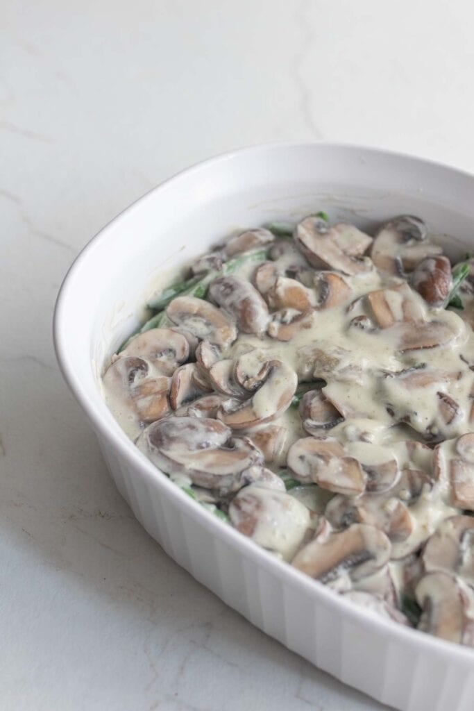 A casserole dish with green beans topped with mushroom cream sauce.