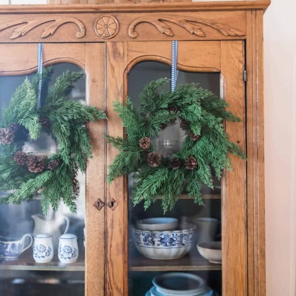 greenery wreaths hung with ribbon on an antique hutch for farmhouse Christmas tour