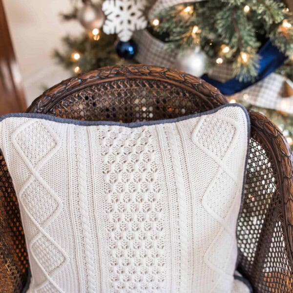 pillow made from a white sweater with blue piping on a wood chair with a Christmas tree in the background