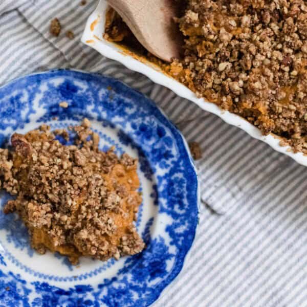 healthy sweet potato casserole recipe with pecan topping on a blue and white antique plate and a baking dish with the remaining sweet potato casserole in a baking dish behind