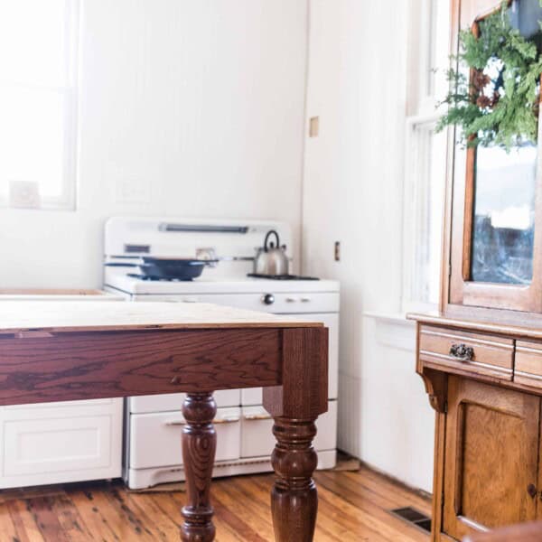 farmhouse kitchen during renovation with a table island, wooden hutch, and antique stove in the background