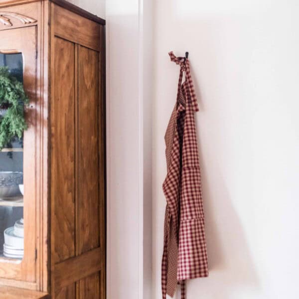 diy reversible apron on a hook next to a wooden china cabinet with a wreath