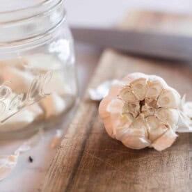 head of garlic with the top cut off with a jar of peeled garlic cloves in a jar to the left.