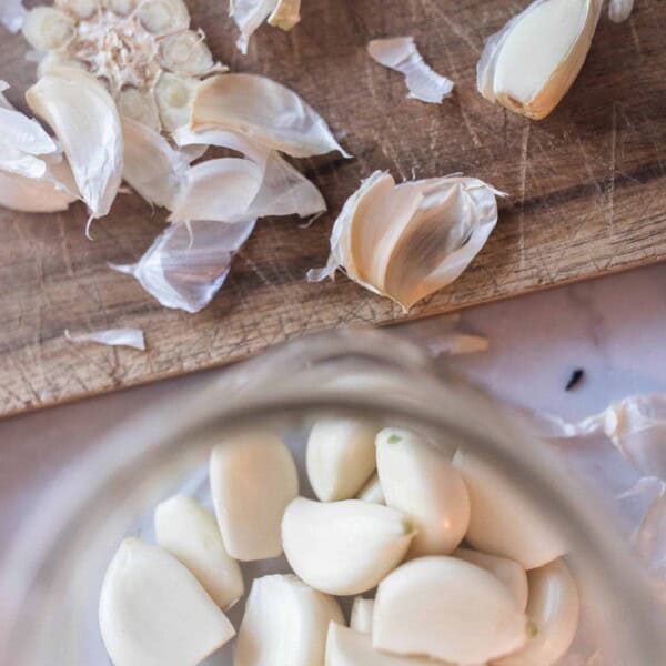 peeled whole garlic cloves in a jar with a cutting board with garlic peels above it