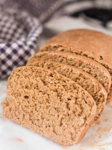 einkorn sandwich bread sliced on a stove top with a blue and white checked towel in the background