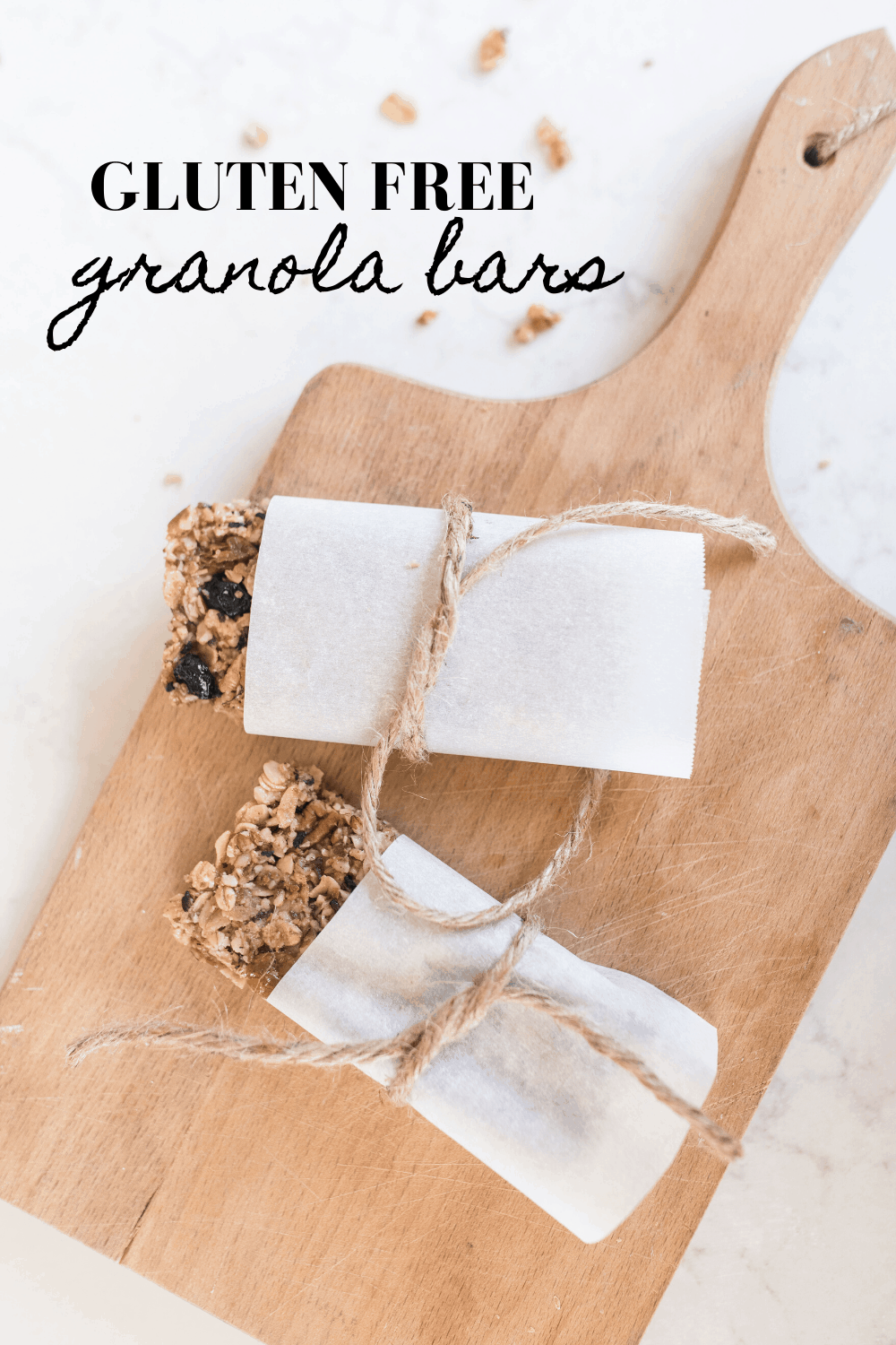 two homemade granola bars wrapped in parchment paper and tied with twine on a wood cutting bar