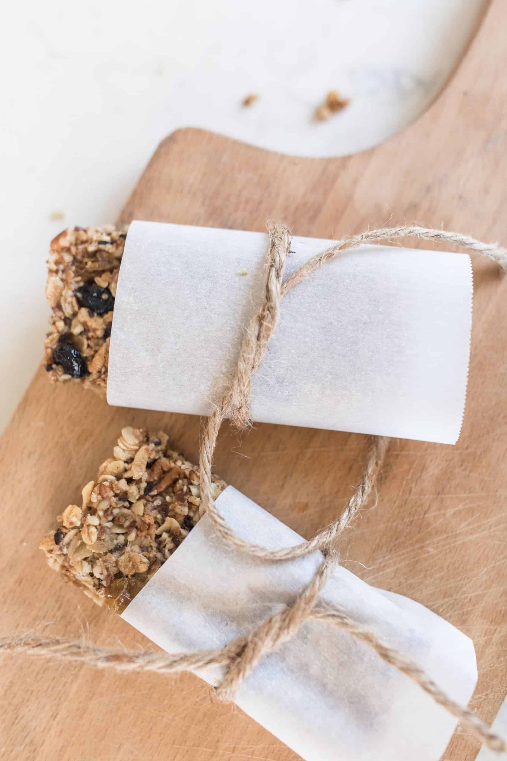 rustic granola bars wrapped in parchment paper and tied with twine on a cutting board.