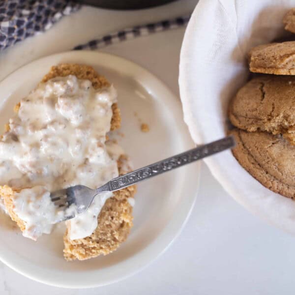 sourdough biscuits smothered in sausage gravy on a white plate. A bowl of sourdough biscuits to the right