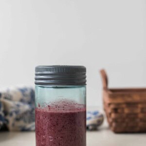 Fermented Blueberry Balsamic Dressing in a glass jar with a tin lid, basic and towel in the background