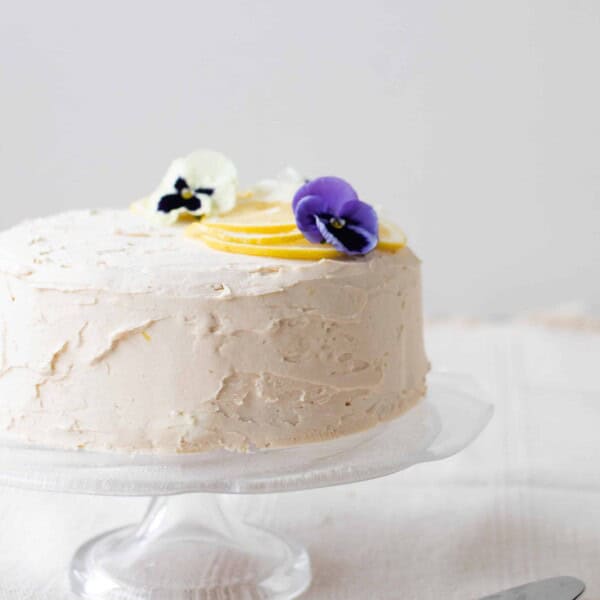 gluten free lemon cake with white lemon icing topped with lemons and edible flowers.