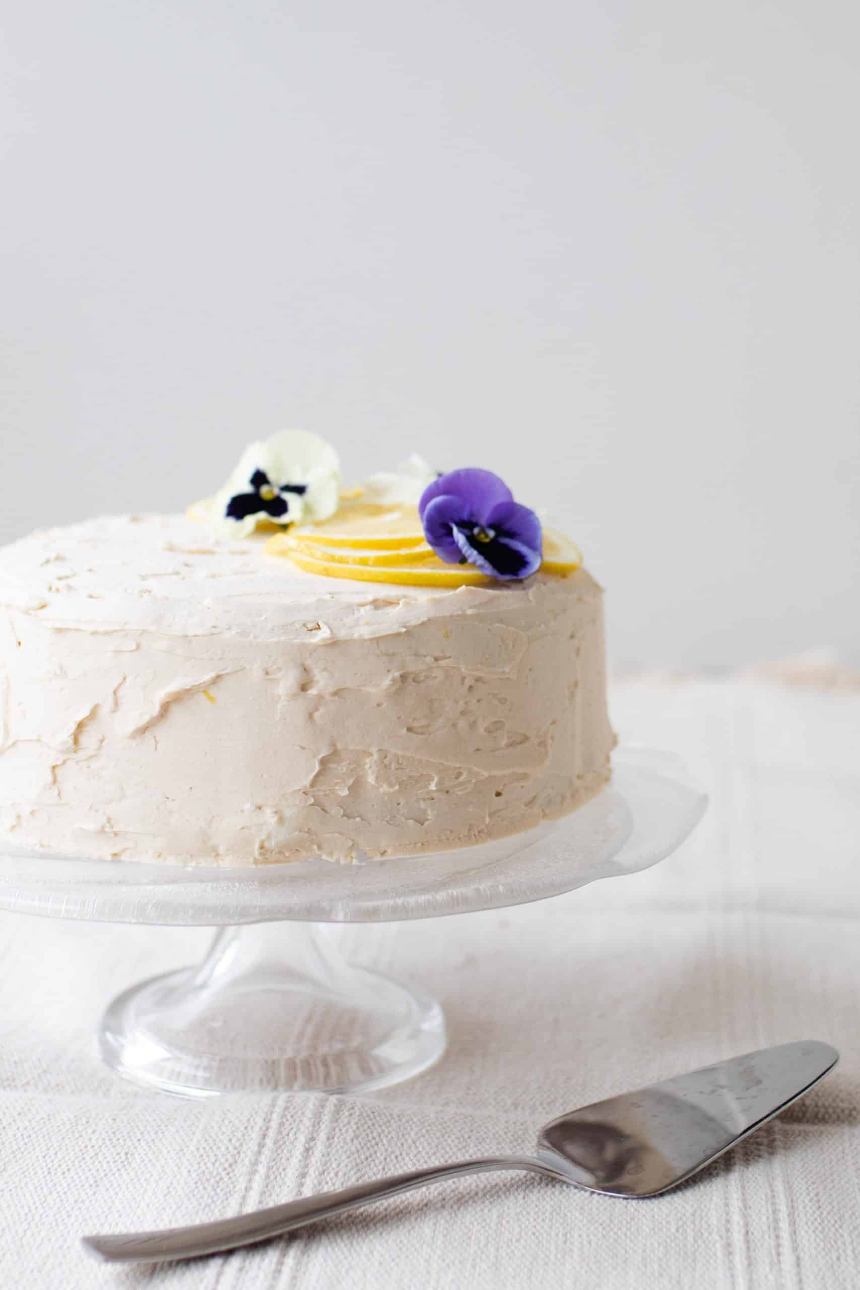 gluten free lemon cake with white lemon icing topped with lemons and edible flowers.