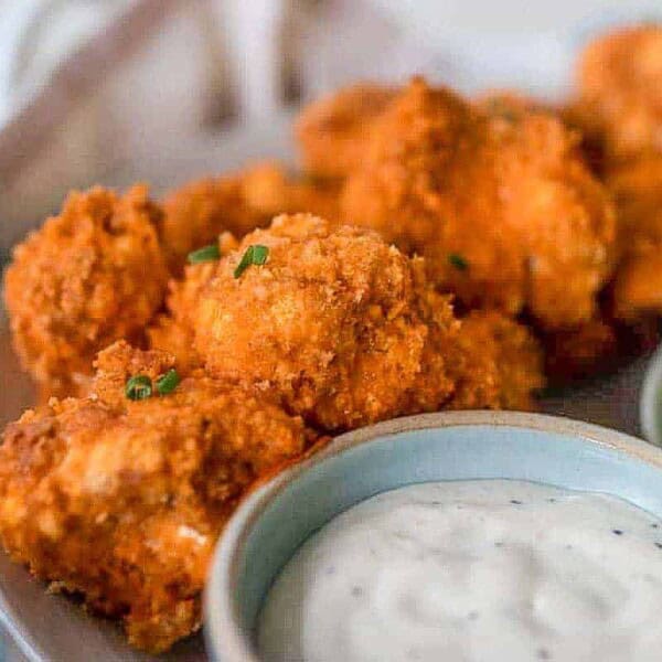 close up picture of buffalo cauliflower bites in a gray plate with dipping sauce