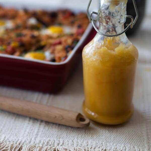 fermented hot sauce in a glass bottle with a swing top lid. A baking dish with hash in the background