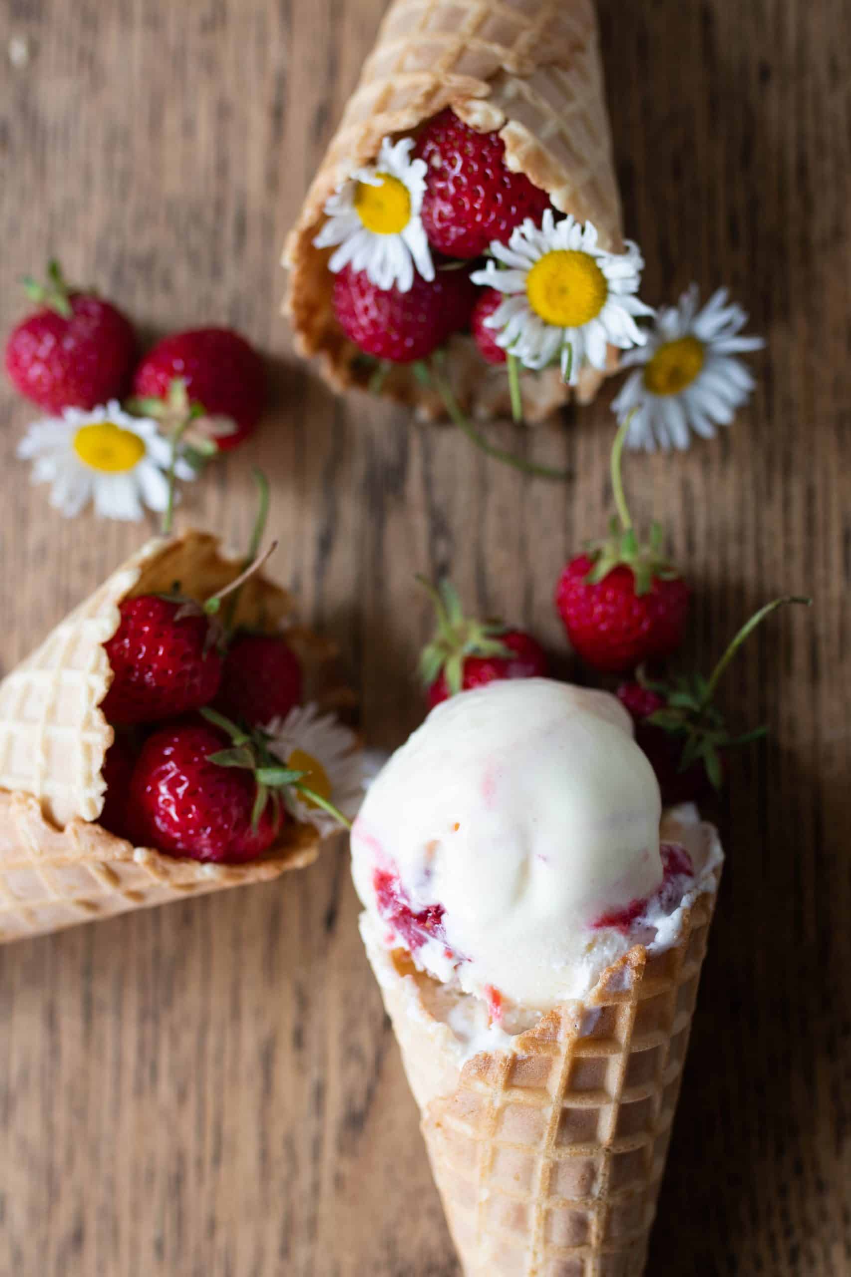 strawberry cheesecake cheese ice cream in a cove with two more cones filled with strawberries with flowers.