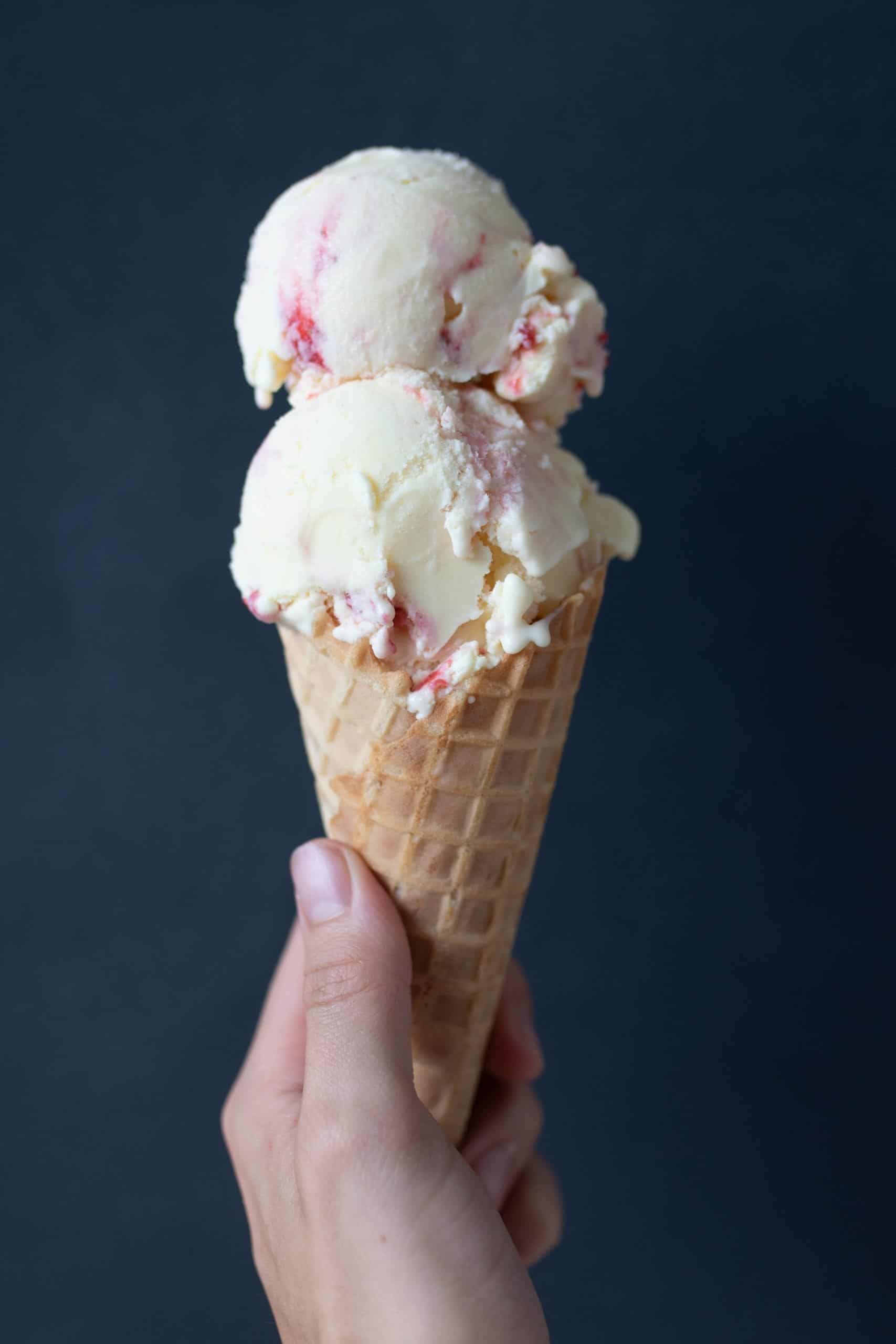 hand holding a cone with two scoop of strawberry cheesecake ice cream